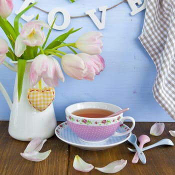 Fresh tea in a colourful cup and tulips in a vase