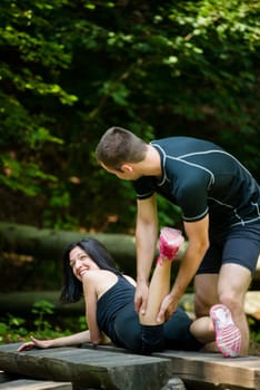 Relax after sport - man massaging calf of his friend outdoor - woman lies on bench