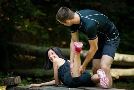Relax after sport - man massaging calf of his friend outdoor - woman lies on bench