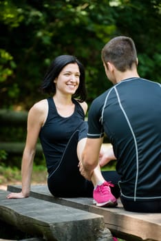 Young man gives massage of calf to smiling woman after jogging