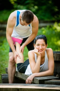 Man gives massage of calf to his girlfriend after sport training - woman lies on bench