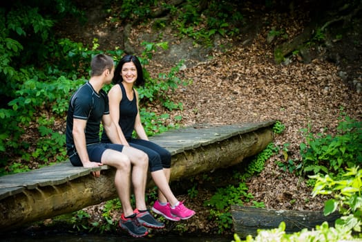 Young sport couple relaxing after sport training on foot bridge in nature