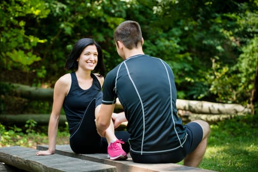Young man gives massage of calf to smiling woman after jogging
