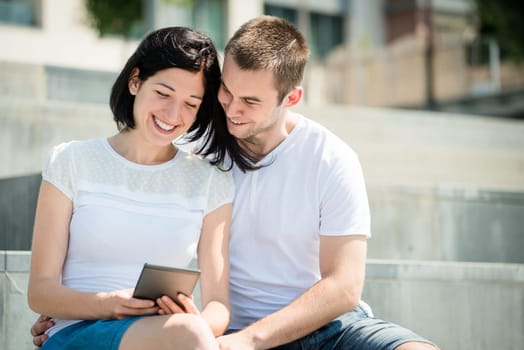 Young happy couple smiling over something in tablet - outdoor
