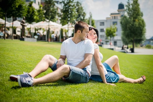 Young couple sitting on grass, leaning with backs and smiling over shoulder