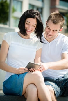 Young happy couple smiling over something in tablet - outdoor