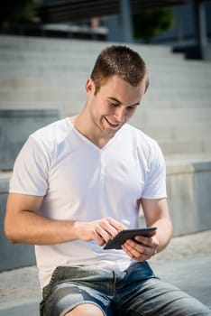 Young man reading book on electronic book-reader in urban environment