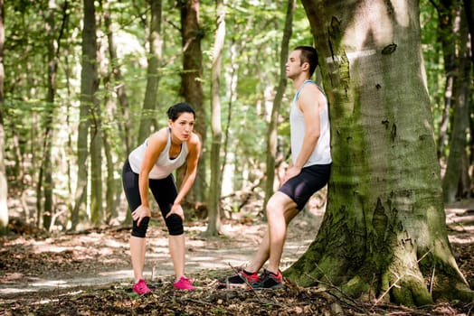 Young couple resting after jogging in nature, man leans against tree