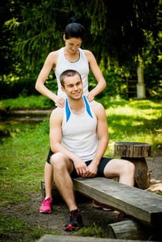 Young woman massaging shouders of her friend after sport training in nature