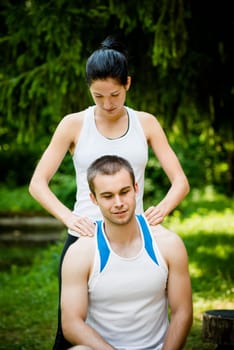 Young woman massaging her friend after sport training in nature
