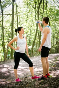 Young couple relaxing after jogging in nature, man drinking water