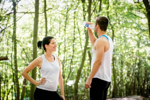 Young couple relaxing after jogging in nature, man drinking water