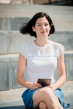 Young woman reading book on electronic book-reader in urban environment