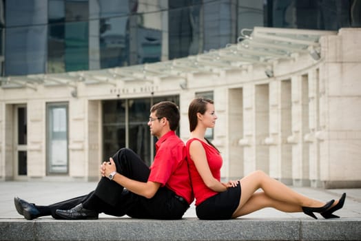 Young business couple relaxing leant with backs on street
