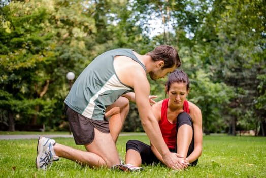 Sport injury - young fitness woman holding her ankle  with pain, man is helping