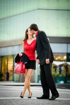 Young business couple dressed in red kiss and welcome each other on street