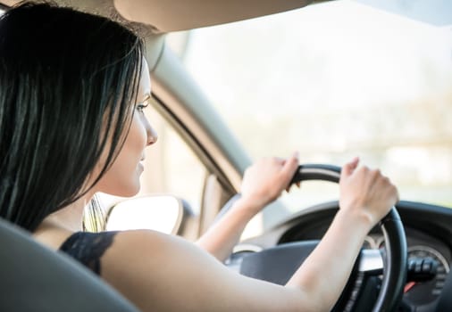 Young beautiful black-haired woman driving car - rear view