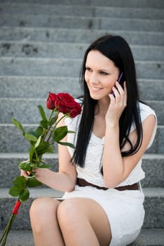 Young beautiful woman with red roses calling with mobile phone