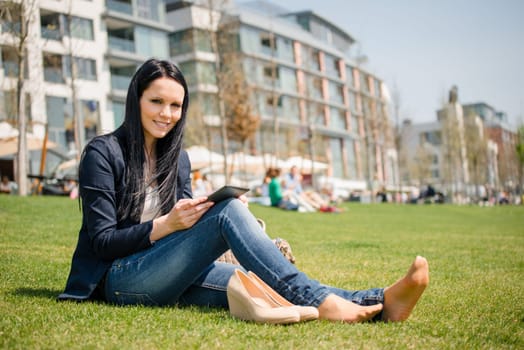 Young woman reading book on electronic book-reader outdoor