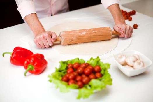 Chef is rolling dough for a italian pizza with pepperoni and mushrooms