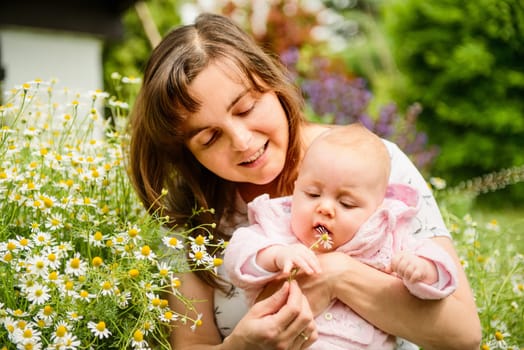 Happy mother with small baby in herb chamomile garden