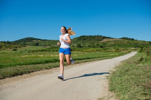 Beautiful teenage girl jogging in nature on sunny day with blue sky