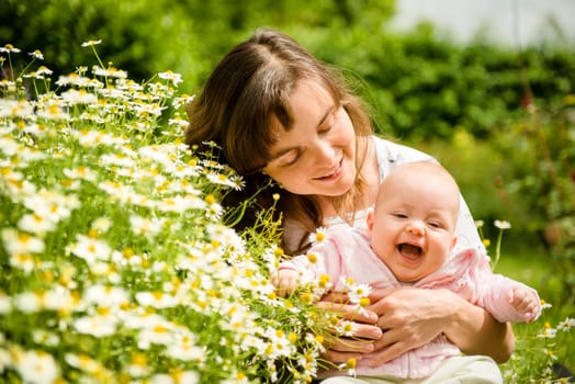 Happy mother with smiling baby in nature (chamomile around)