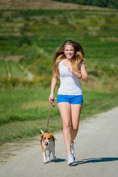 Beautiful teenage girl jogging with her pet (beagle dog) in nature