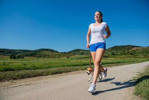 Beautiful young woman jogging with her pet (beagle dog) in nature