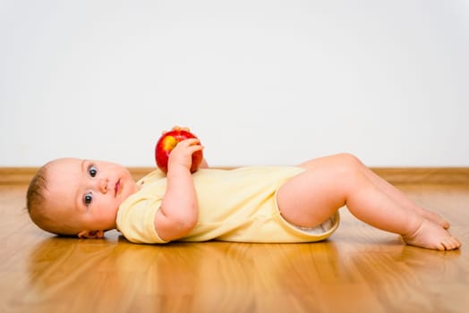 Baby holding apple lying on floor - healthy lifestyle