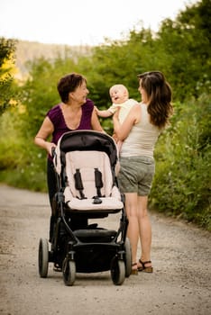 Generations - grandmother with her daughter and her granddaughter outdoor on walk with stroller