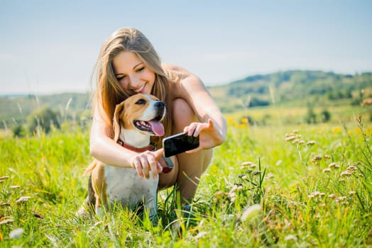 Young smiling woman showing something to her dog on smart-phone, outdoor in nature