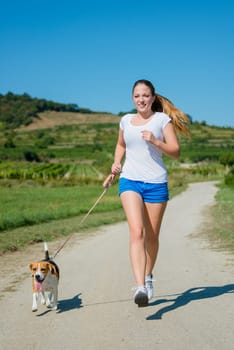 Beautiful teenage girl jogging with her pet (beagle dog) in nature