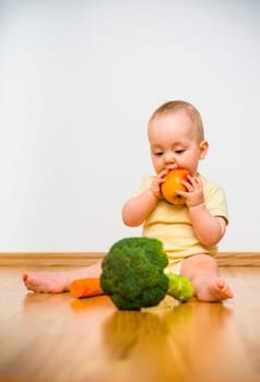 Healthy living. Baby eating fruit and vegetables - sitting on floor
