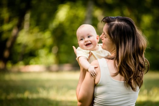 Happy mother holding her baby on hands outdoor in nature