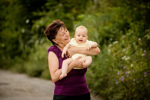 Grandmother with grandchild - senior woman holding her granddaughter outdoor in nature
