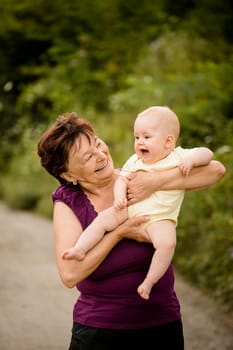 Grandmother with grandchild - senior woman holding her granddaughter outdoor in nature