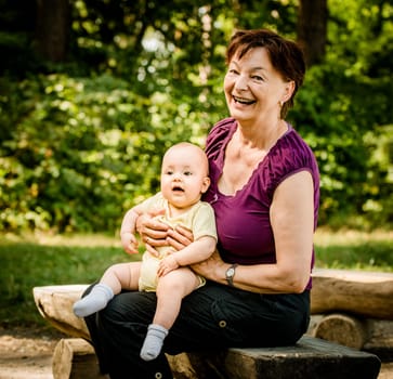 Grandmother with grandchild - senior woman sitting with her granddaughter on bench outdoor in nature