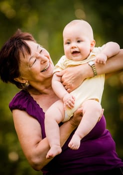 Grandmother with grandchild - senior woman holding her granddaughter outdoor in nature