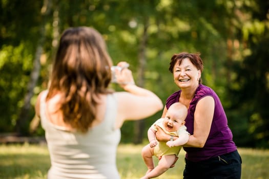 Mother taking photo of grandmother holding her granddaughter - outdoor in nature