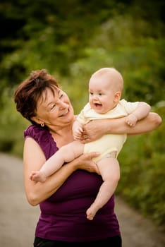 Grandmother with grandchild - senior woman holding her granddaughter outdoor in nature