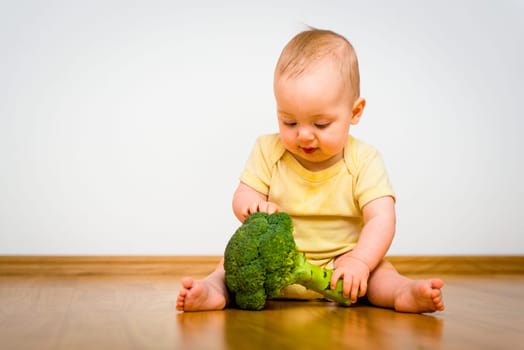 Cute baby exploring broccoli - sitting on floor indoors