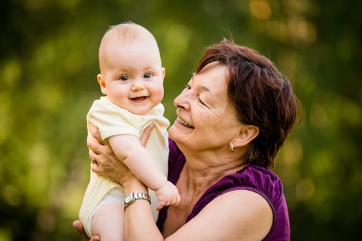 Grandmother with grandchild - senior woman holding her granddaughter outdoor in nature