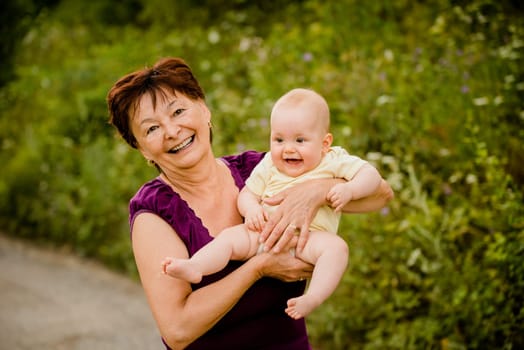 Grandmother with grandchild - senior woman holding her granddaughter outdoor in nature