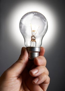 Mans hand holding a light bulb against grey background