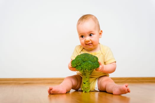 Cute baby eating broccoli at home - unhappy expression
