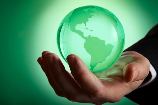 Glass green globe glowing in palm of businessmans hand
