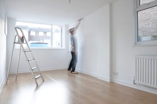man decorating a room with ladder and paint pot in foreground