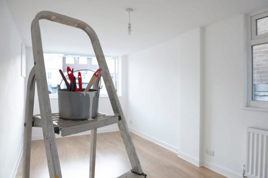 ladder with paint pot and brushes standing in empty room