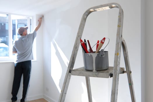 man decorating a room with ladder and paint pot in foreground